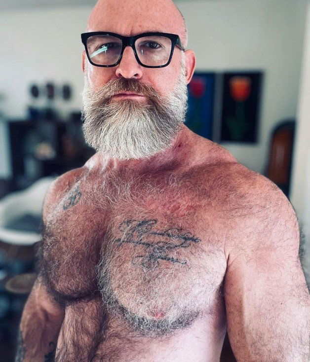 Photo by Nickplus33 with the username @Nickplus33, who is a verified user,  May 30, 2024 at 2:33 AM and the text says '#bald #beard #specs #hairy #hairychest #ink #granddaddy #daddy #muscled'