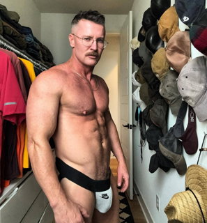 Photo by Nickplus33 with the username @Nickplus33, who is a verified user,  July 3, 2024 at 2:06 AM and the text says '#toned #dilf #specs #bulge #jockstrap #stache #chain'
